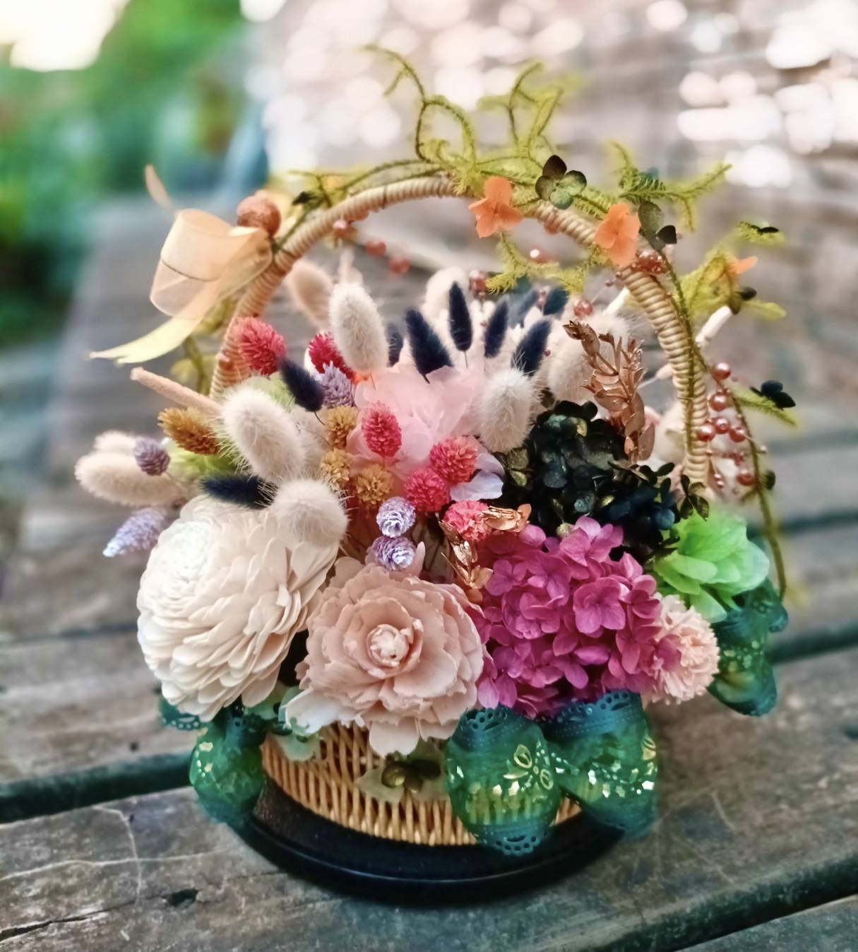 高坂嘉玲によるプリザーブドフラワーの花かご。白やピンクの花、紫の花房、緑のリボンが組み合わされています。